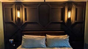 Un dormitorio con cabecera de madera oscura, dos almohadas de colores claros y una mesita de noche con lámpara.