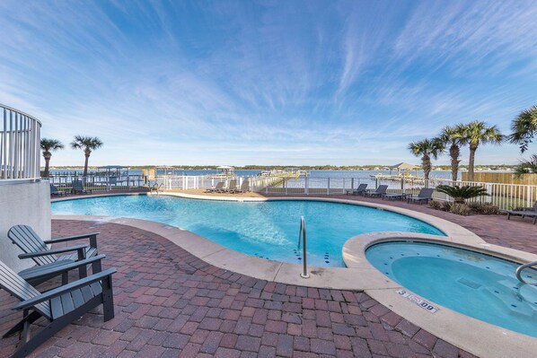 A pool area with lounge chairs and a view of the water.
