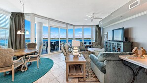 Een ruime woonkamer met uitzicht op zee, een eettafel, een bank en een televisie.