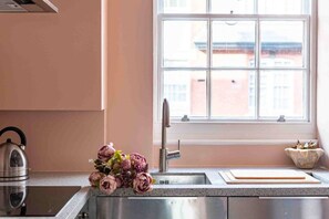 Cozinha com pia de aço inoxidável, chaleira e um vaso de flores.