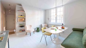 A modern, well-lit dining area with a round table, chairs, and a green sofa. - Open plan Chelsea apt for 2 nr King’s Road (London)