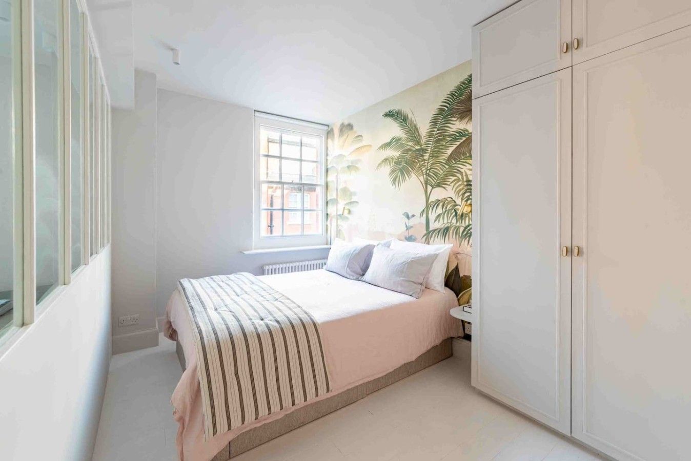 A bedroom with a bed, a window, a radiator, and a wardrobe.