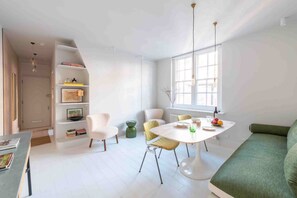 A modern living room with a dining area, a sofa, a table with chairs, and a bookshelf.