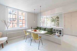 A modern kitchen with a dining area, white cabinetry, and a view of the city through large windows. - Open plan Chelsea apt for 2 nr King’s Road (London)