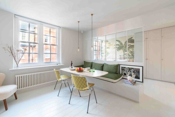 A modern kitchen with a dining area, white cabinetry, and a view of the city through large windows.
