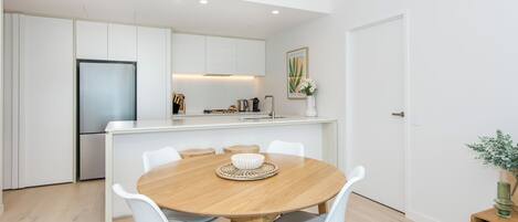 Una cocina moderna con muebles blancos, un refrigerador de acero inoxidable y una isla central con pileta y encimera.
