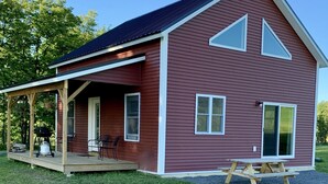 A red barn with a covered porch, a picnic table, and a grill.