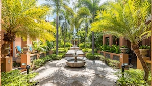 Une cour intérieure avec une fontaine centrale, entourée de palmiers et de plantes en pot.