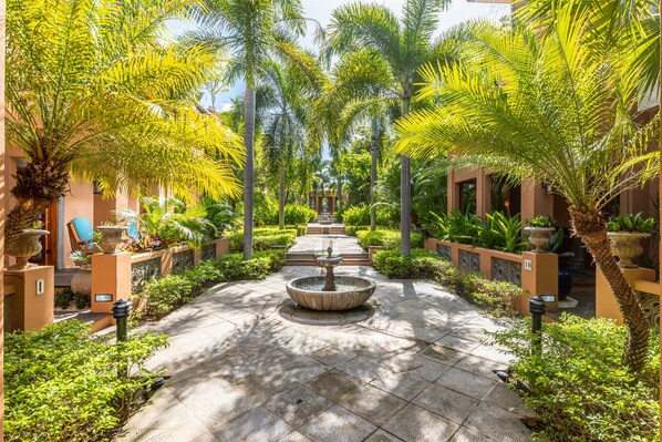A courtyard with a central fountain, surrounded by palm trees and potted plants.