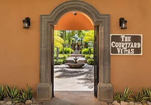An entrance with an archway leading to a courtyard with a fountain and greenery.