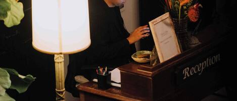 A reception desk with a lamp, a vase with flowers, and a framed document on the desk.