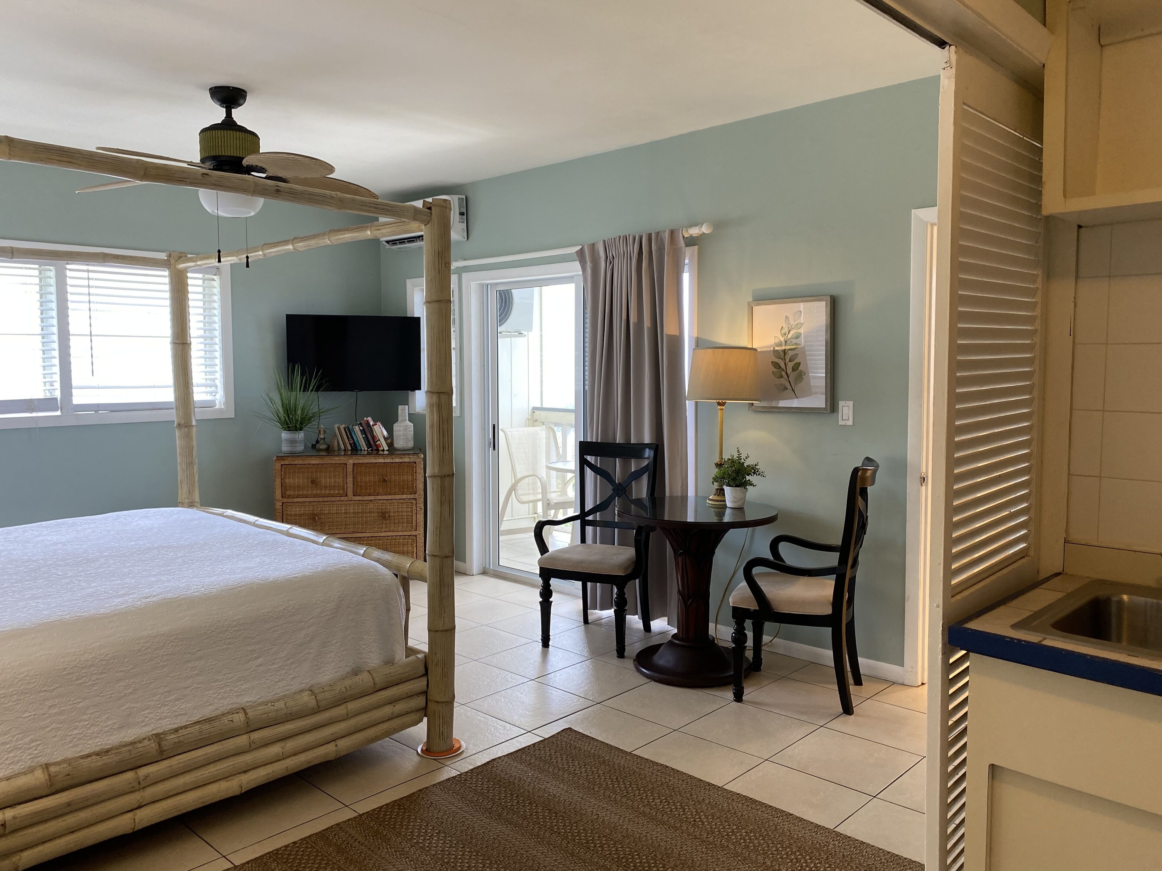 Un dormitorio con cama con dosel, una zona de comedor con mesa y sillas, un televisor y una ventana con persianas.