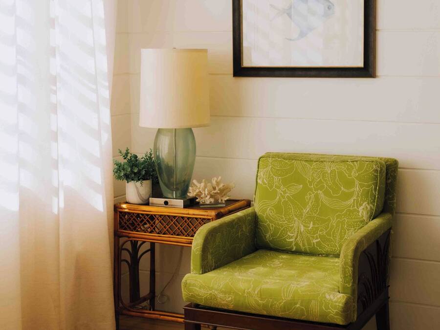 A room with a green armchair, a table with a white object, a lamp, and a framed picture on the wall.