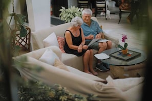 Una pareja sentada en un sofá con una mesita de vidrio, rodeada de plantas y muebles de interior.