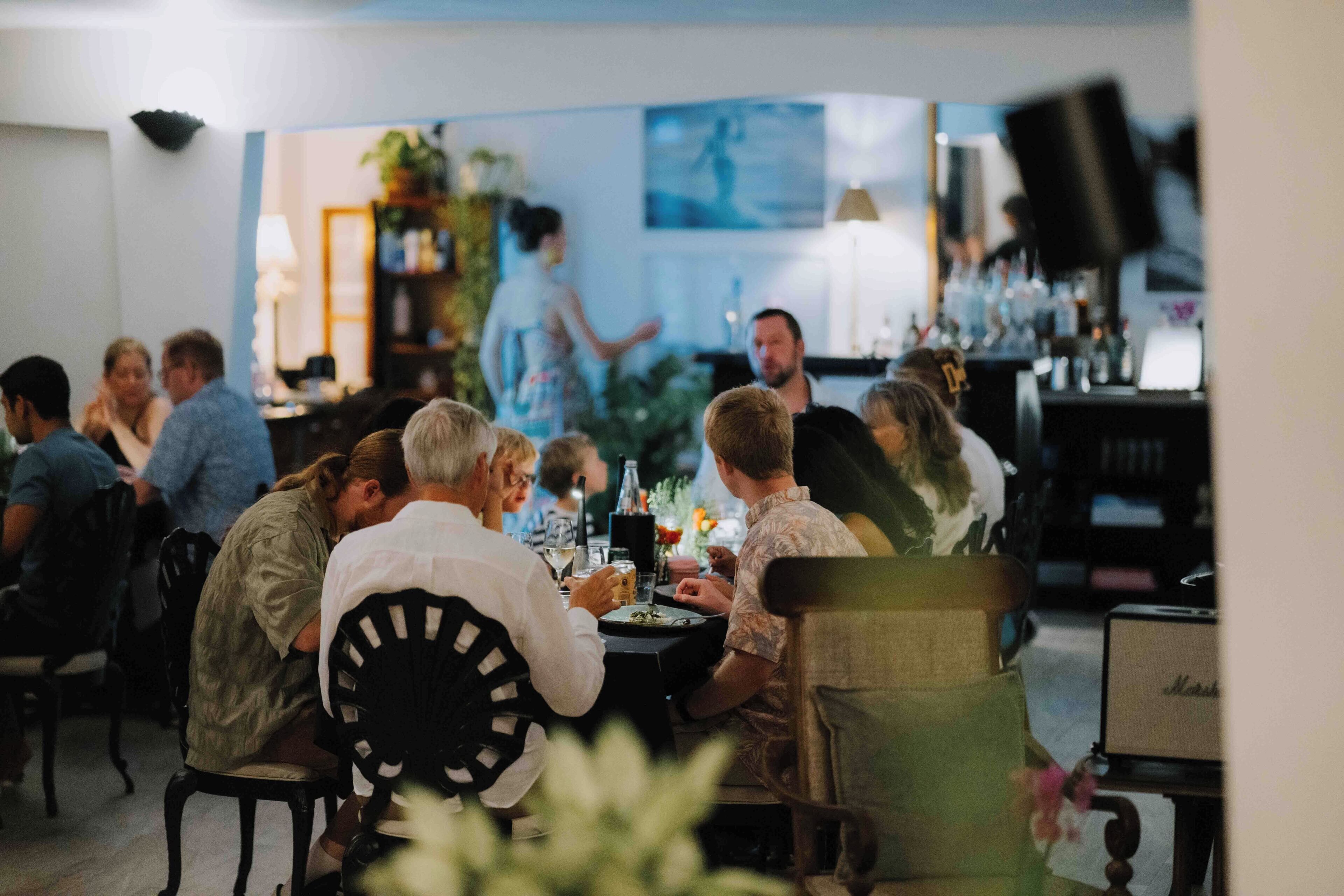 Een groep mensen dineert in een restaurant, met een bar op de achtergrond.