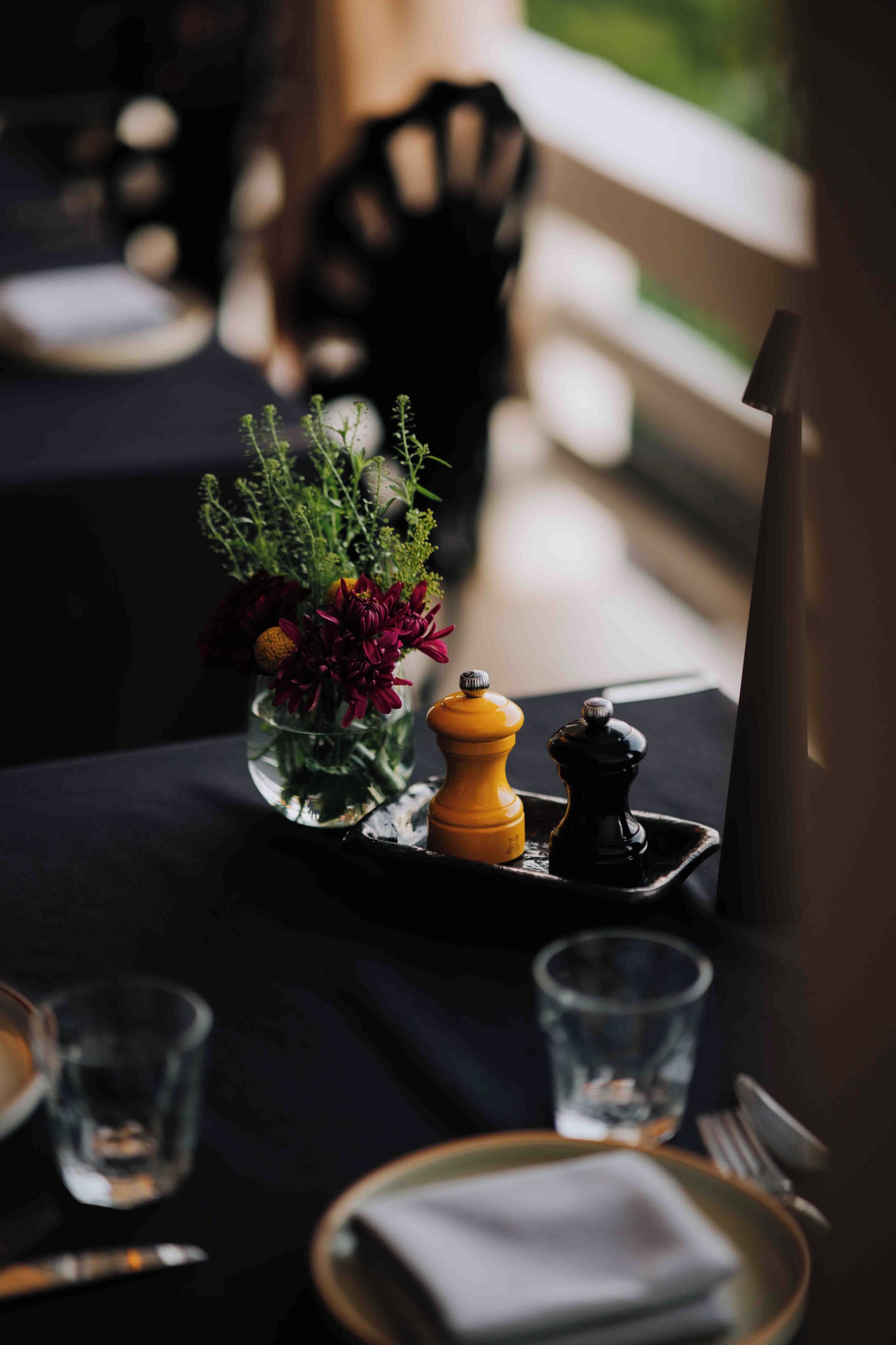 A table set with a glass vase of flowers, a pepper grinder, and a salt shaker.
