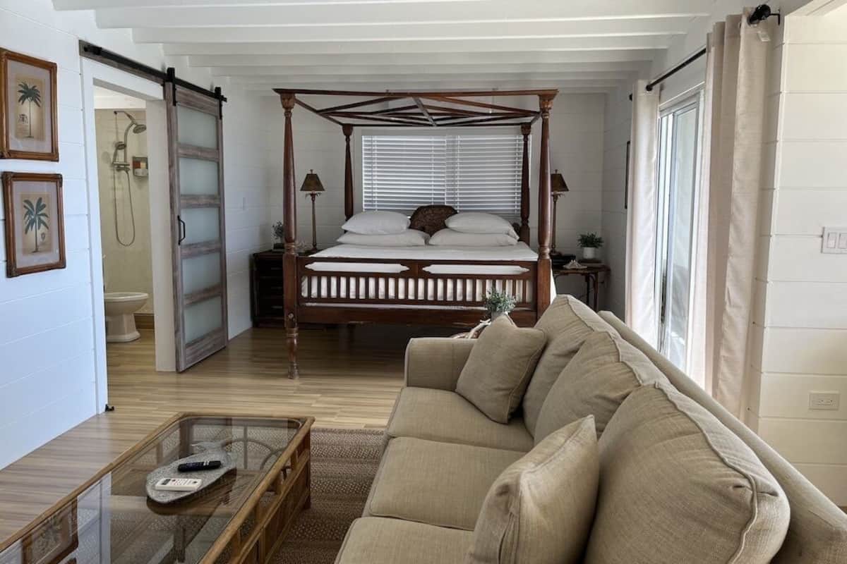 A bedroom with a four-poster bed, a sofa, a glass coffee table, and a sliding door leading to a bathroom.