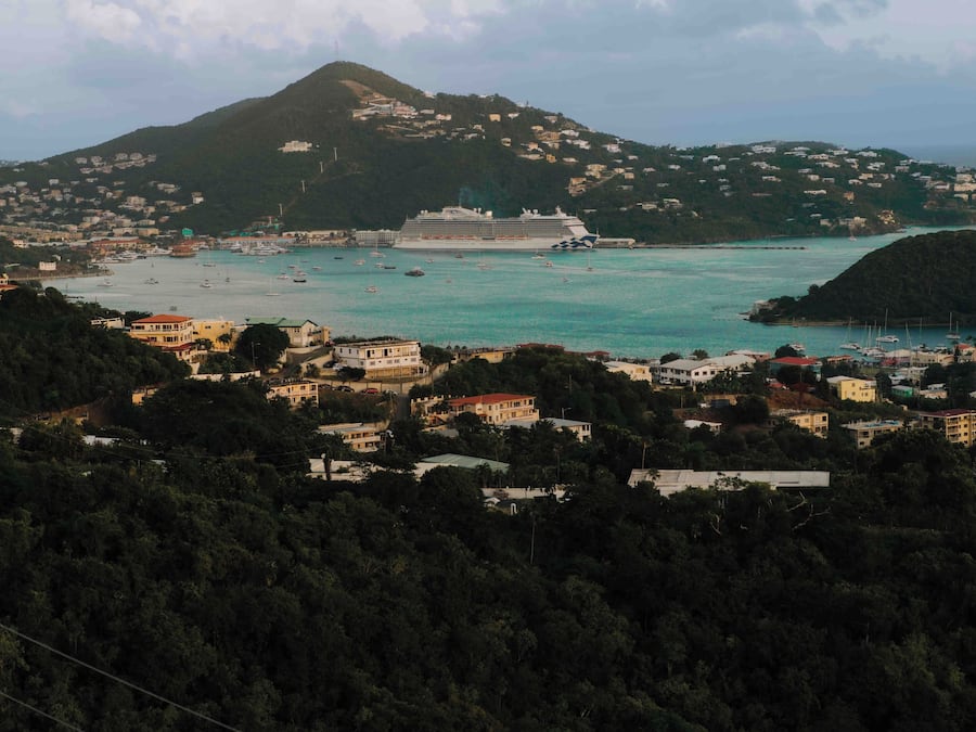 A coastal town with a cruise ship docked, surrounded by residential buildings and a mountainous backdrop.