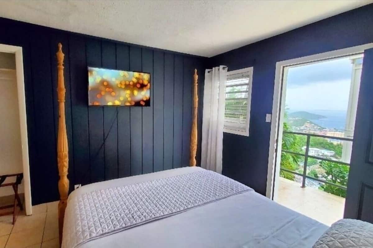 A bedroom with a bed, a TV mounted on the wall, a balcony with a view, and a door leading to a closet.