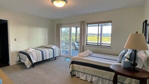A bedroom with two beds, a window with a view of the outdoors, a lamp on a bedside table, and a carpeted floor. - Marsh view double decker ultimate privacy off the main paths. 862 Fiddlers Ridge (Fripp Island)