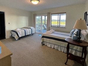 A bedroom with two beds, a window with a view of the outdoors, a lamp on a bedside table, and a carpeted floor.