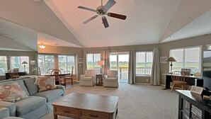 A spacious living room with a ceiling fan, large windows, a sofa, a coffee table, and a TV stand. - Marsh view double decker ultimate privacy off the main paths. 862 Fiddlers Ridge (Fripp Island)