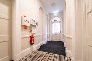 A hallway with a fire extinguisher, a smoke vent, and an exit sign.