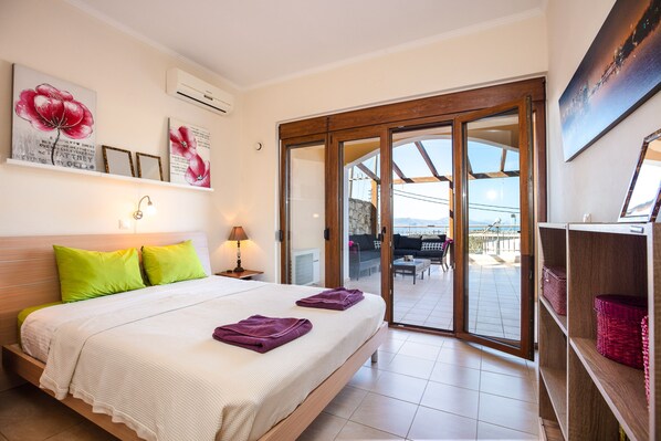 Ein Schlafzimmer mit einem Bett, Kissen, einem Nachttisch und Blick auf einen Balkon.