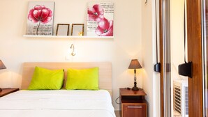 Habitación de hotel impecable con cama, dos almohadas verdes, mesita de noche con lámpara y una obra de arte floral en la pared.