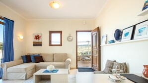 Una sala de estar con un sofá seccional color beige, una mesa de centro y un comedor con una mesita y sillas. Hay una puerta que da a un área exterior con vistas al paisaje.