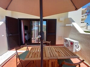Um pátio externo com mesa e cadeiras de madeira, um guarda-sol e um aparelho de ar condicionado.