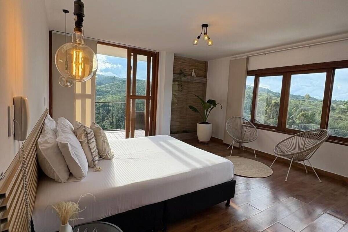 A bedroom with a large bed, a view of the outdoors, a potted plant, and a chair.