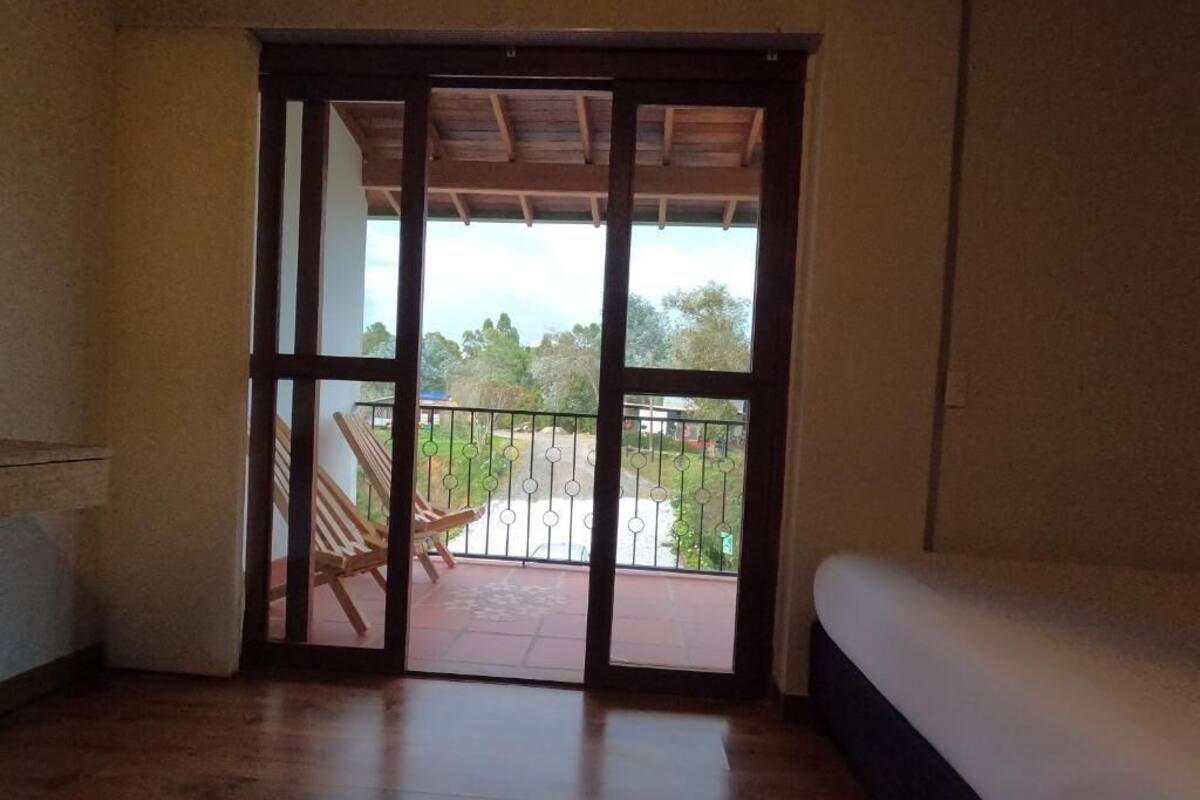 A room with a wooden floor, a bed, and a sliding glass door leading to an outdoor area with a patio and a chair.