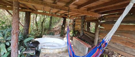 A wooden structure with a hammock, a hot tub, and a garden area with plants and gravel.