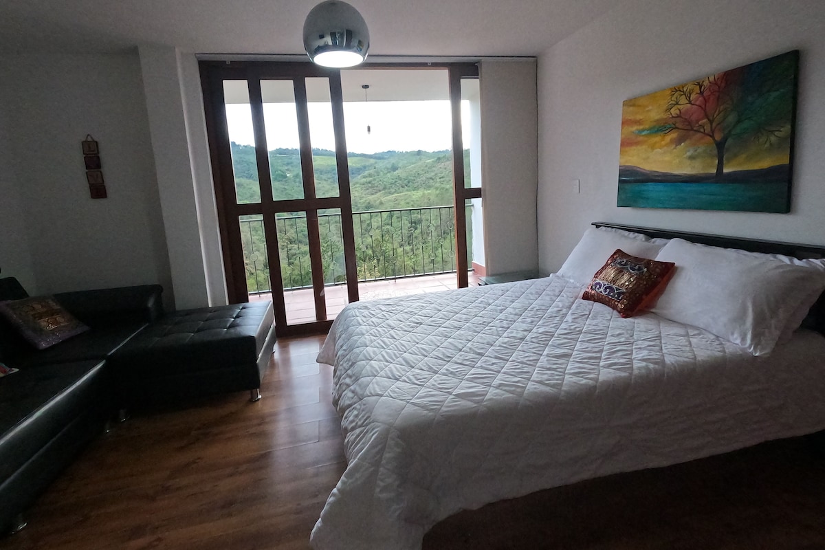 A bedroom with a bed, a sofa, a painting, and a balcony with a view.