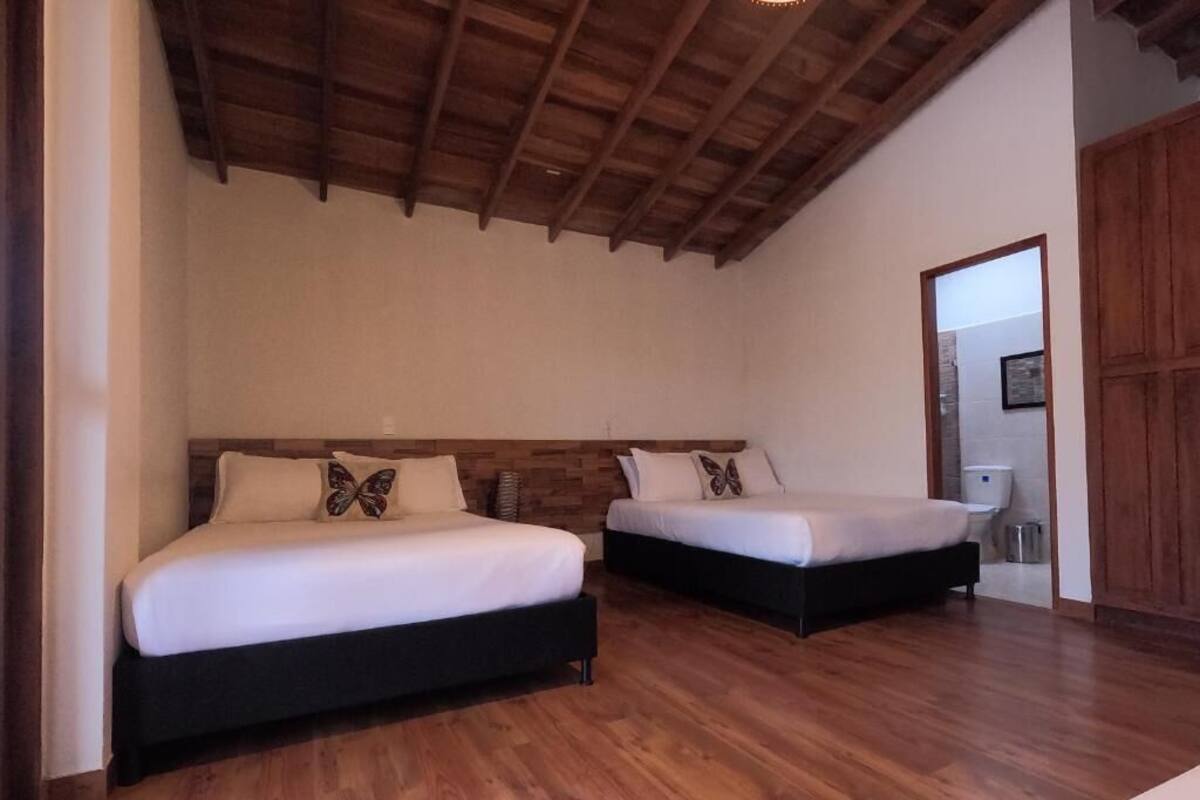 A bedroom with two beds, wooden flooring, a wooden ceiling, and a door leading to another room.