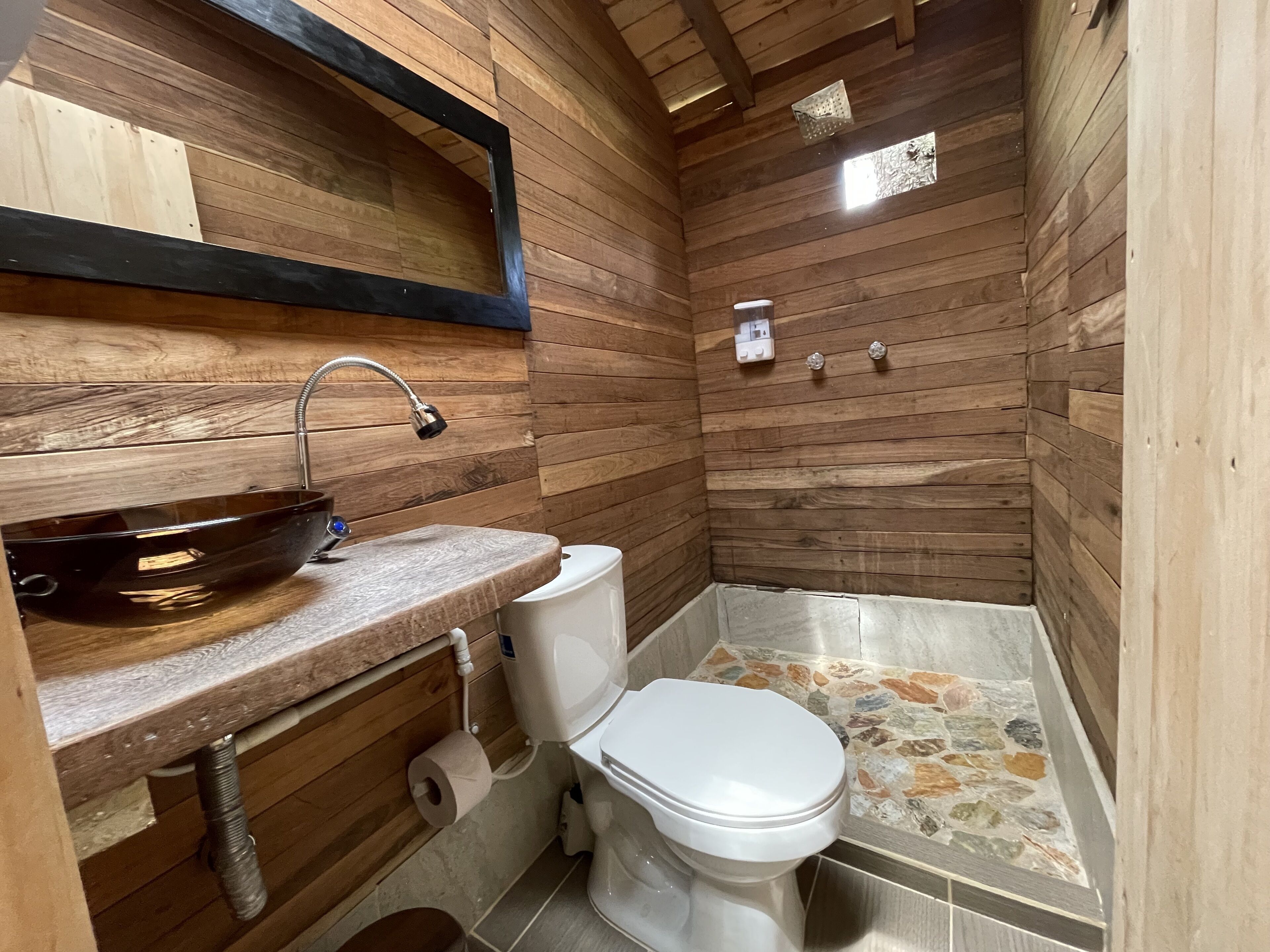 Un baño con paredes y lavamanos de madera, un inodoro y una ducha con mosaicos.