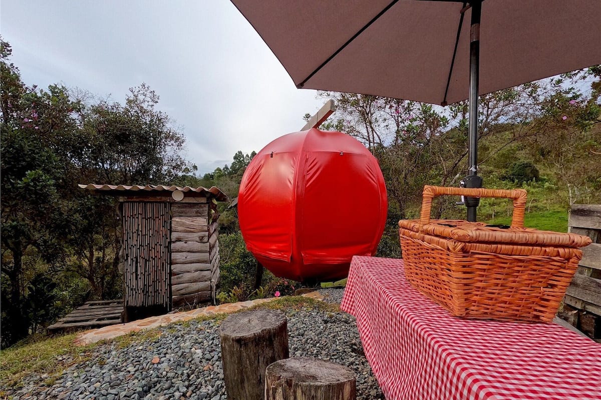 A rustic outdoor setting with a red spherical object, a wooden structure, a wicker basket, and a checkered tablecloth.