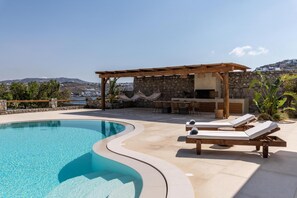 A pool with a curved edge, lounge chairs, a pergola, and a stone wall.