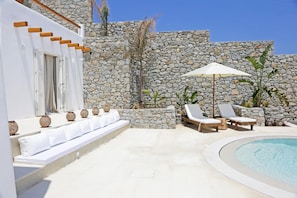 A poolside area with lounge chairs, a small table, and a stone wall.