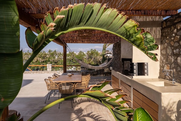 An outdoor dining area with a stone wall, a wooden pergola, and a hammock.