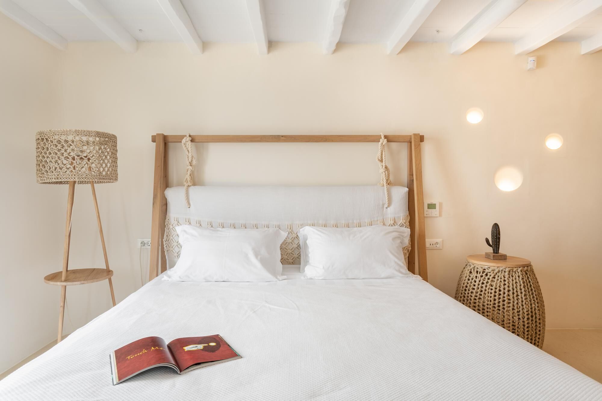 A neatly made bed with a wooden headboard, a bedside lamp, and a small table with a cactus.
