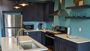 Een moderne keuken met donkerblauwe kastjes, een roestvrijstalen koelkast, een magnetron en een houten vloer.