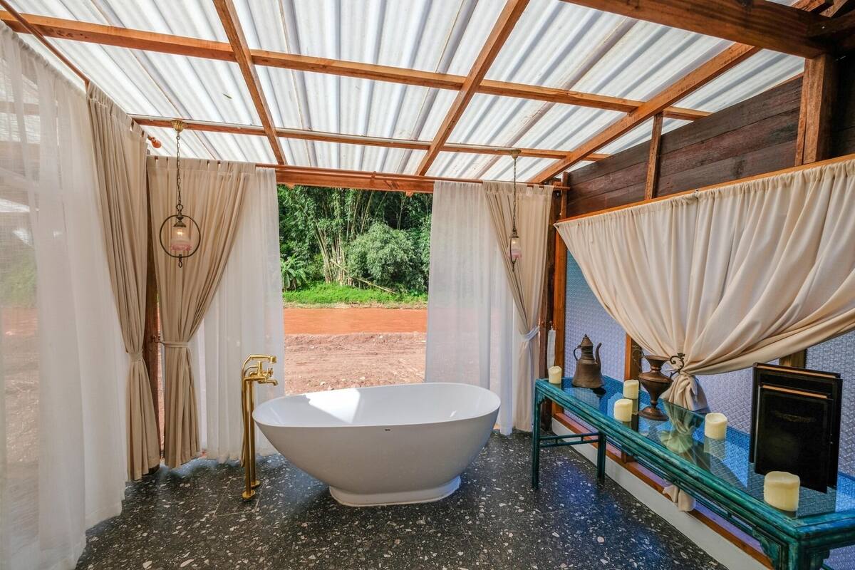 A bathroom with a freestanding bathtub, wooden beams, and a view of greenery outside.