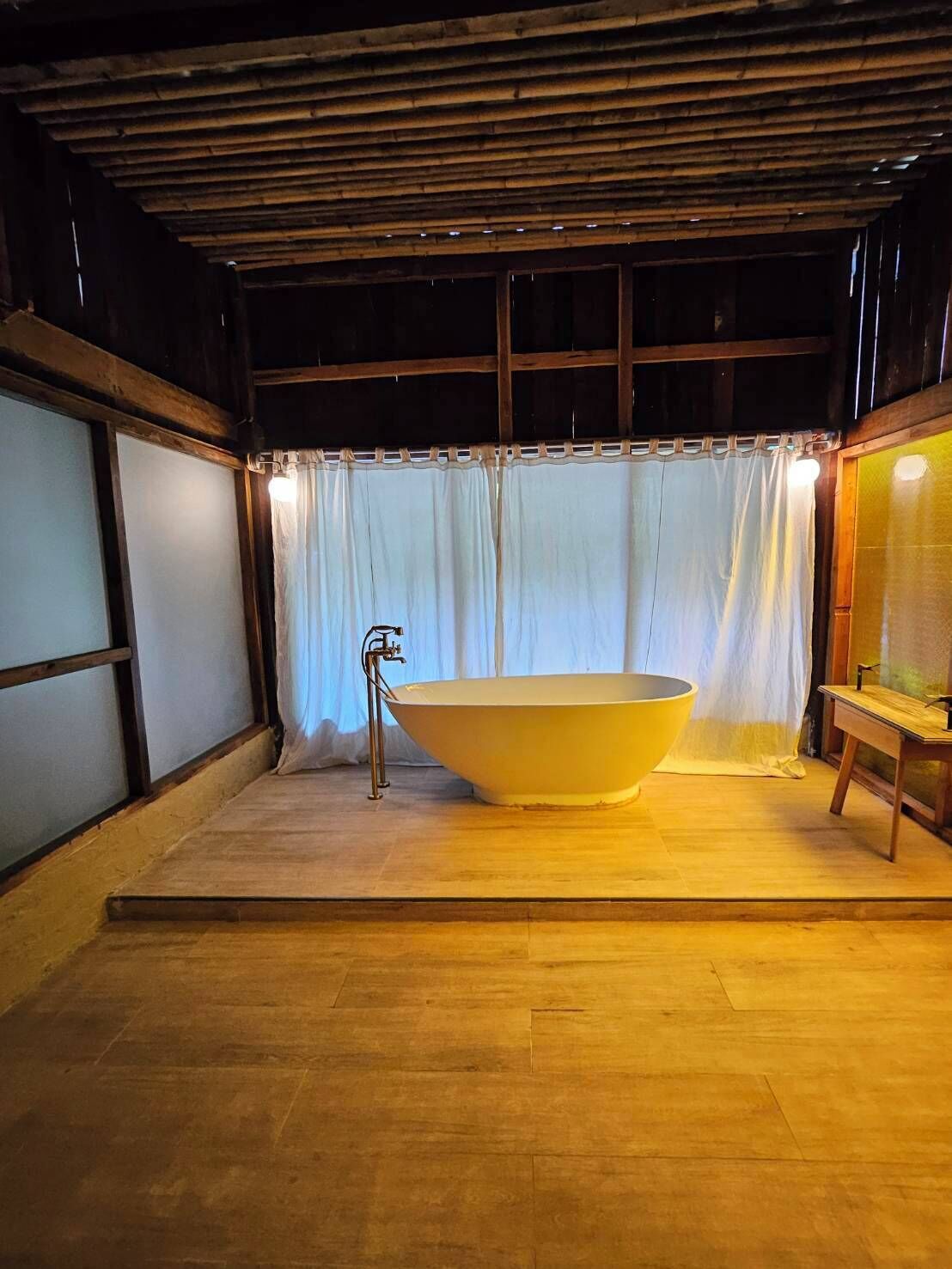 A bathroom with a freestanding bathtub, wooden flooring, and a curtain separating the space.