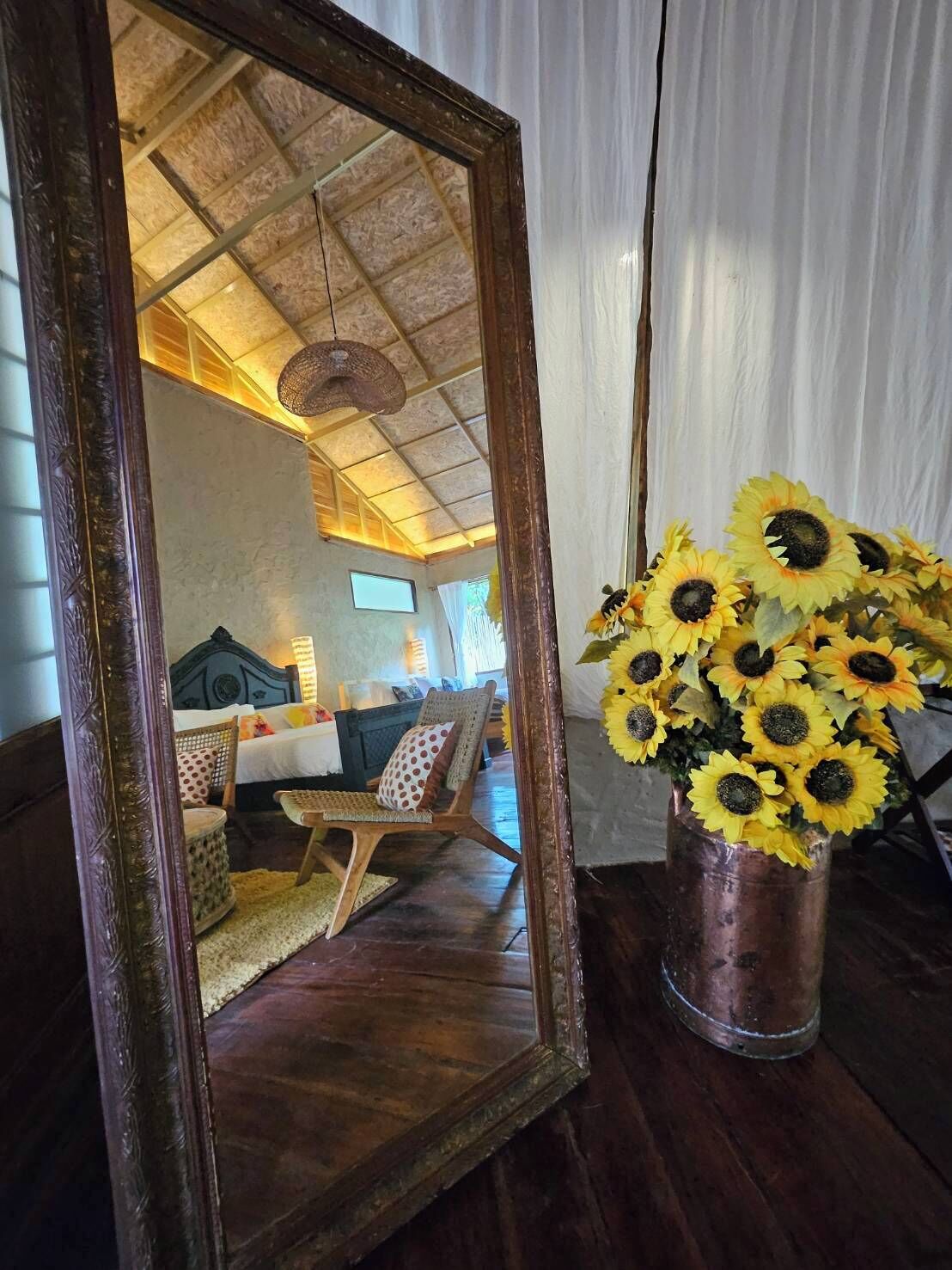 Ein Schlafzimmer mit Holzboden, einem Bett, einem Sessel und einer Vase mit Sonnenblumen.