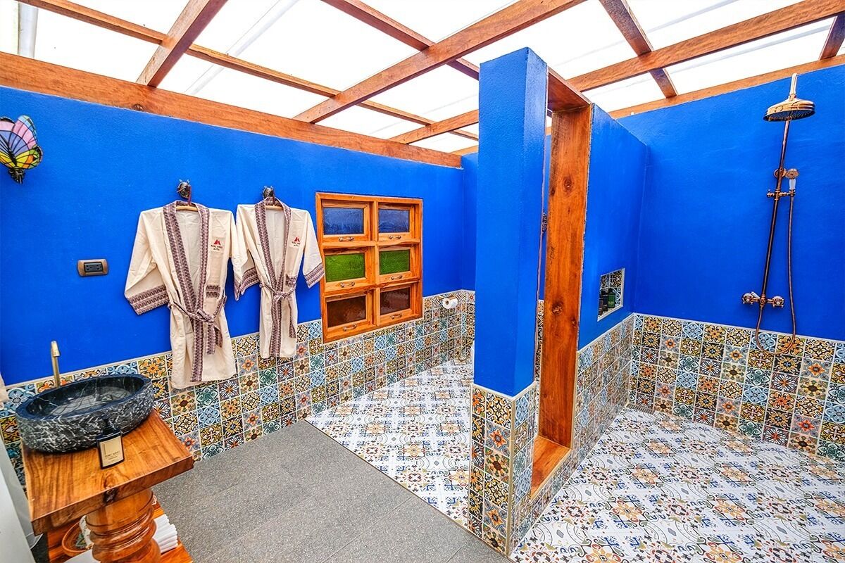 Baño con paredes azules, techo de madera y ducha. Hay dos toallas colgadas en ganchos y una ventana pequeña.