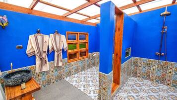 Baño con paredes azules, techo de madera y ducha. Hay dos toallas colgadas en ganchos y una ventana pequeña.