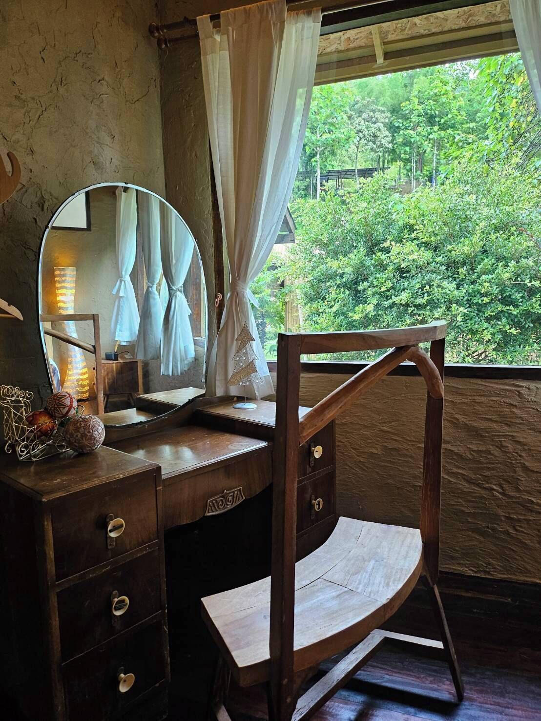 A wooden desk with a mirror, a chair, and a window with curtains.