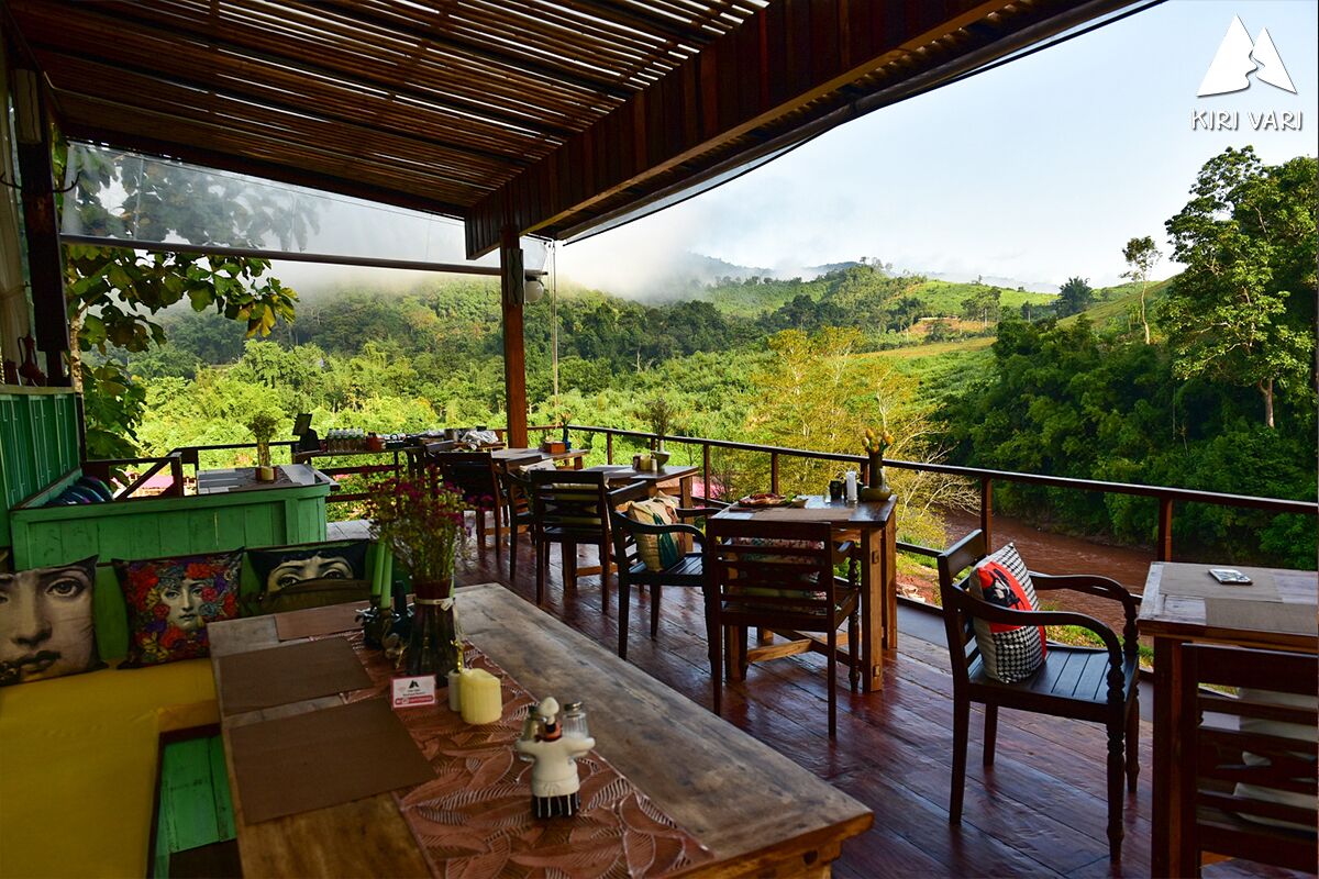 A covered outdoor seating area with wooden furniture and a view of a lush green landscape.
